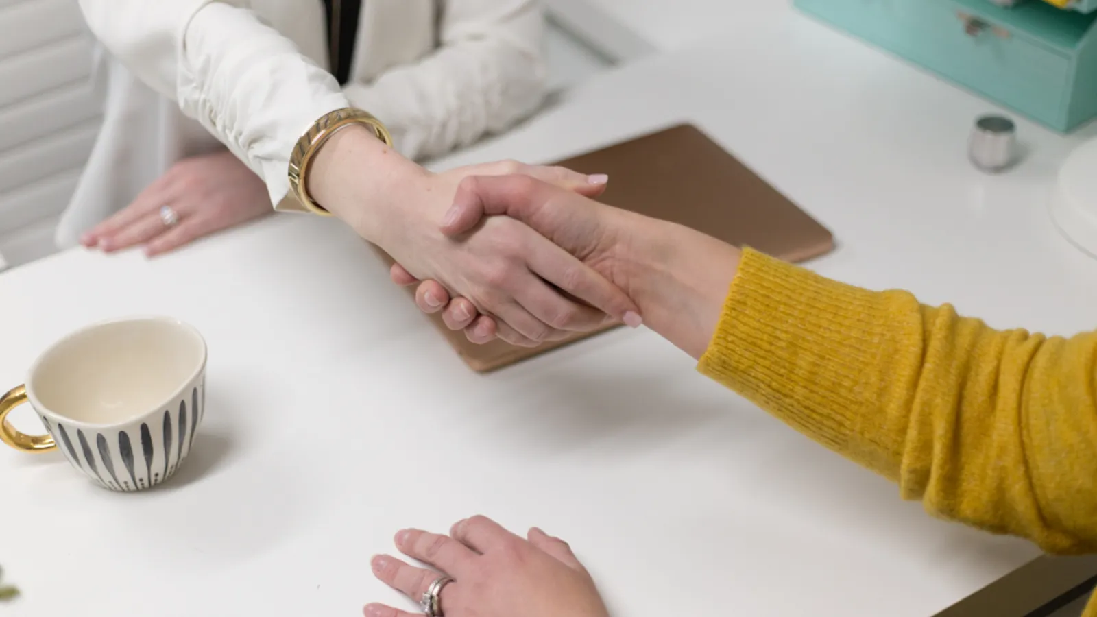 A salesperson and a client shaking hands across a meeting table after agreeing on a deal.
