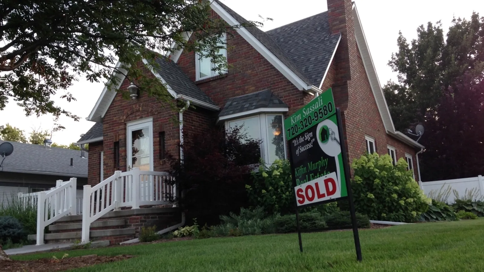 A brick home with a SOLD yard sign on the front lawn.