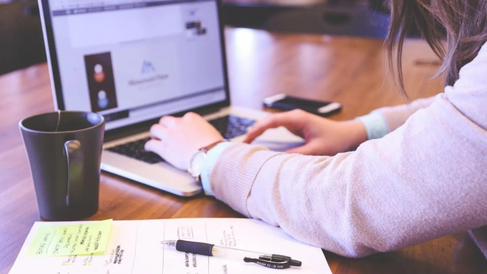 A sales development rep wearing a headset makes calls at a desk with a laptop in an open office.