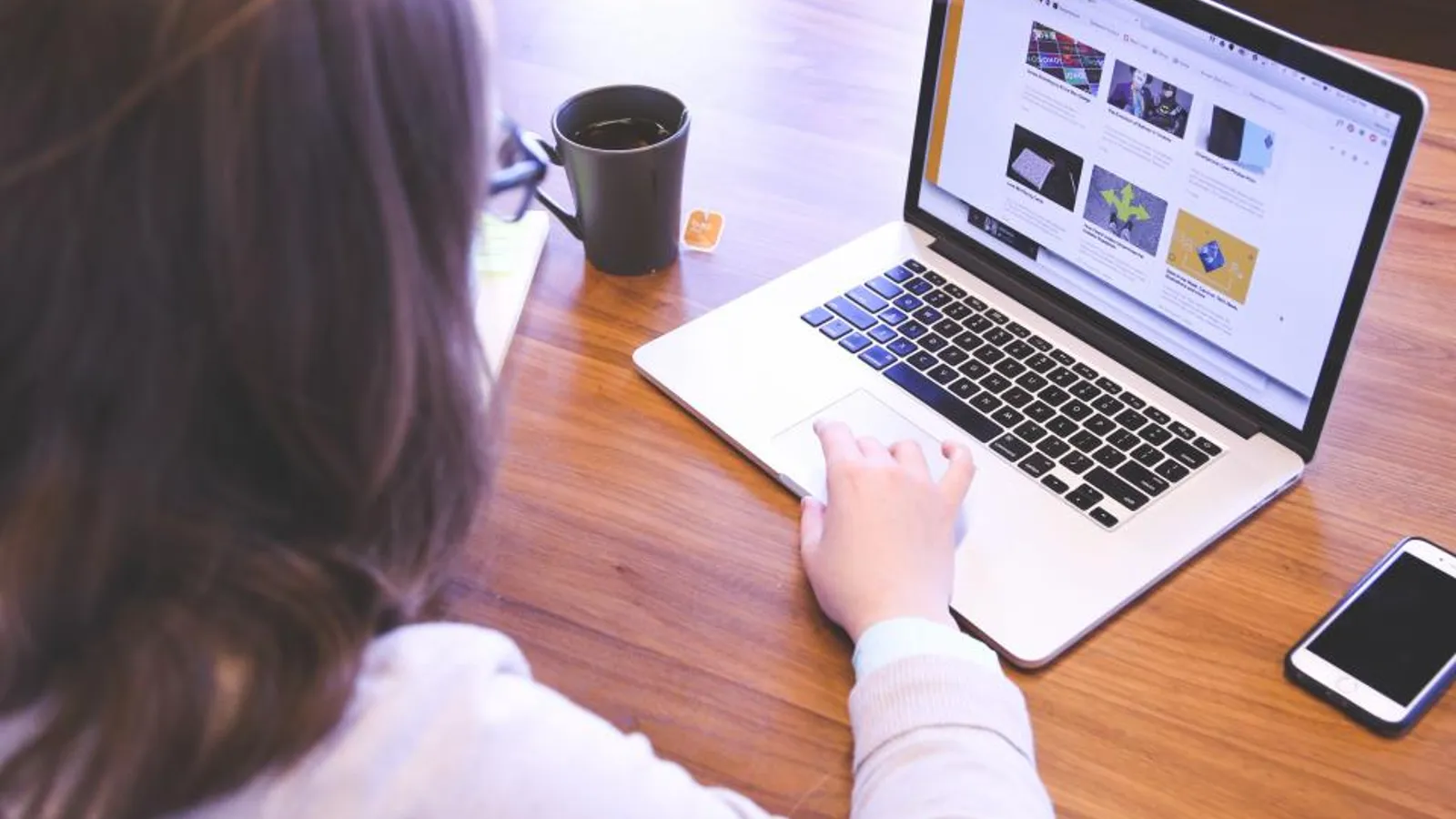 A young sales rep at an office desk building a prospect list on a laptop, with a phone and notepad beside her.