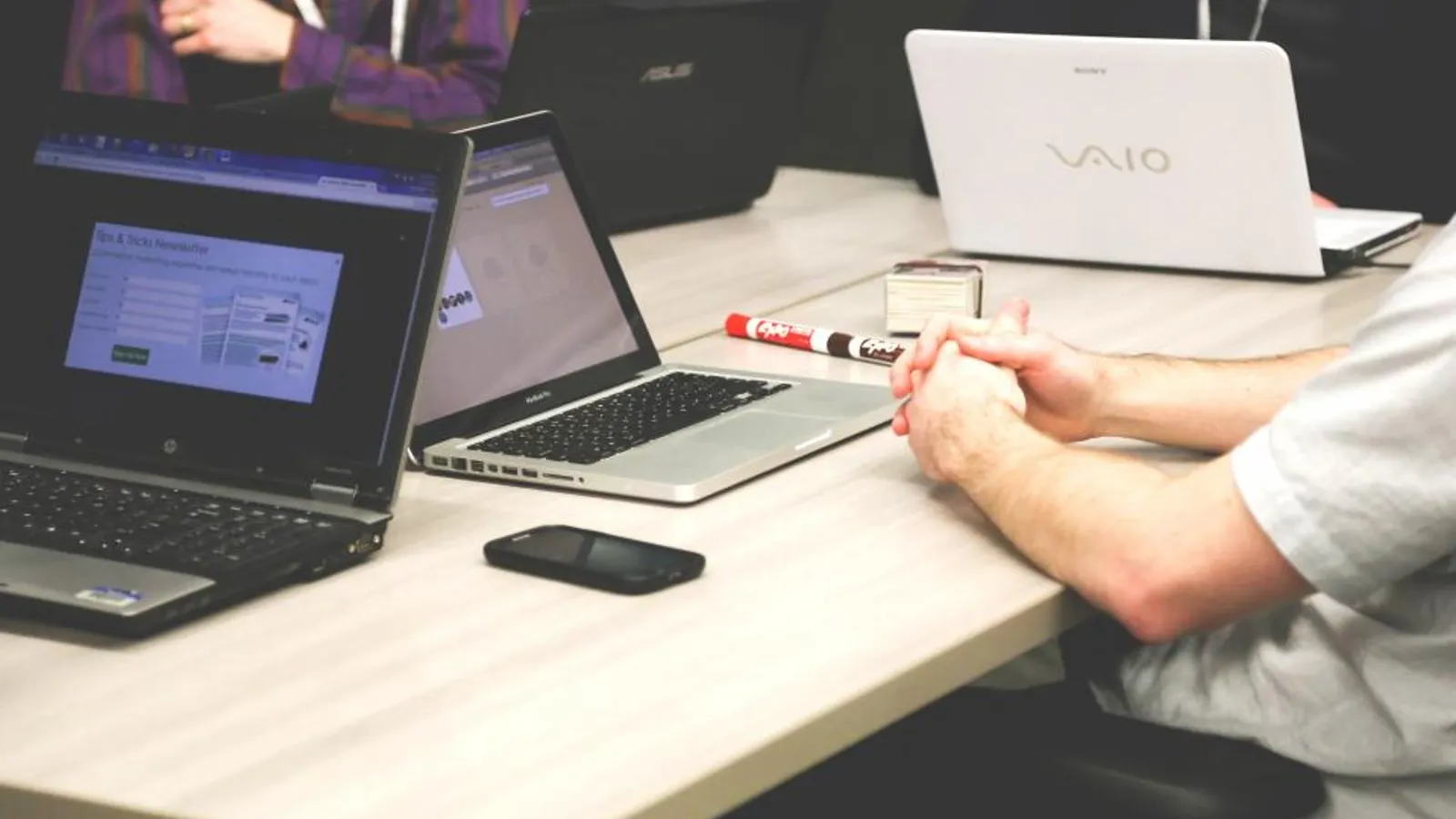 A sales manager coaching a rep at a desk in a busy open office.