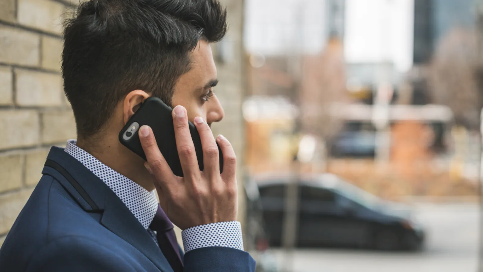 A salesperson wearing a headset makes a phone call at a desk with a printed call list and a cup of coffee.
