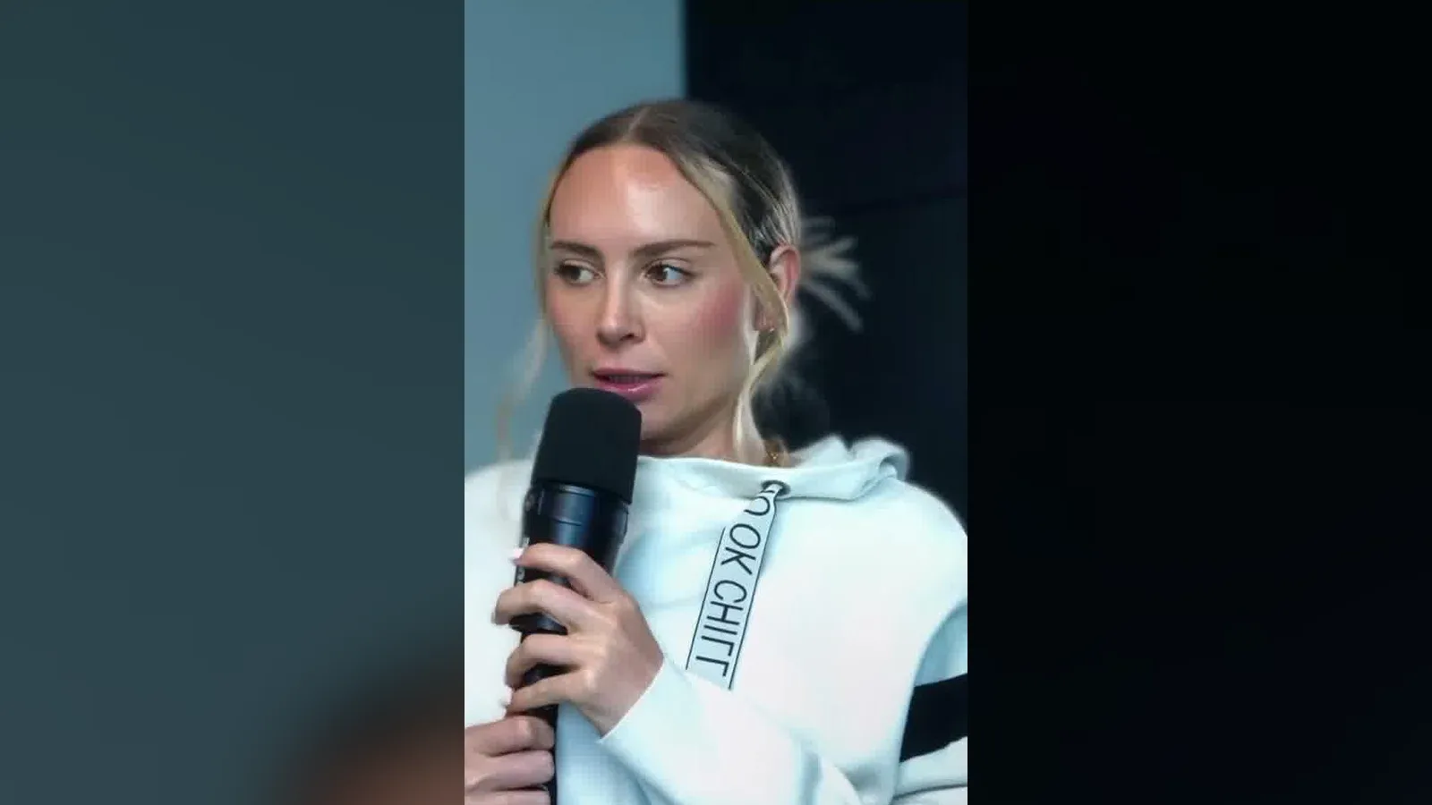 Danielle Lynch in a white hoodie holding a microphone while telling the story of her sales career.