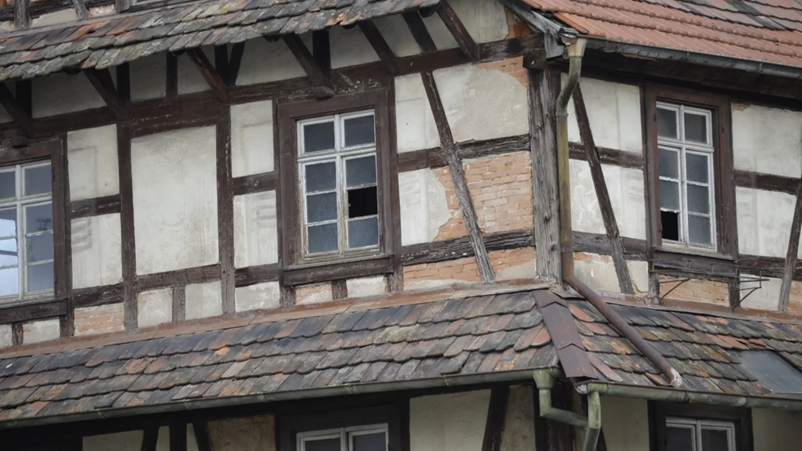 Close view of an old timber-frame house with weathered windows and a worn roof.